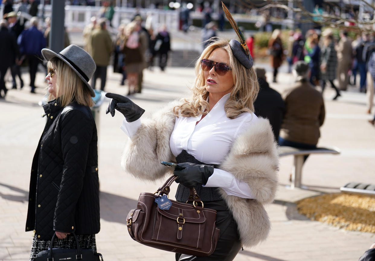 Carol Vorderman, wearing a white shirt with a faux fur shrug around her shoulders, with a fascinator featuring a long feather on her head, arriving on day one of the Cheltenham Festival at Cheltenham Racecourse