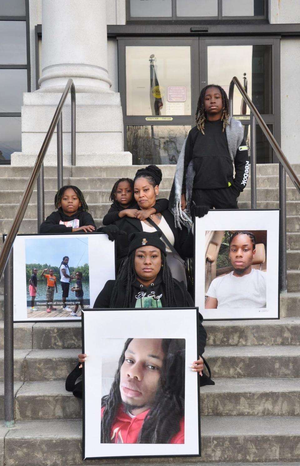 Patricia King and her family holding photos of Elijah Timmons III. Seen in the photo are three of Timmons' four sons: 12-year-old Siir'ziion (far right), 6-year-old Kii'zerriion (middle), and 10-year-old E'miilliion (far left).
