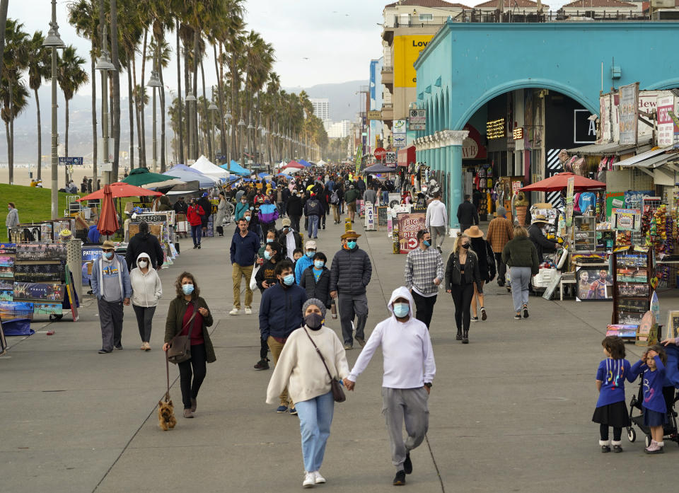 People stroll on the Venice Beach Boardwalk in Los Angeles, Sunday, Dec. 27, 2020. In Los Angeles County, the nation's most populous, county estimates show that about 1 in 95 people are contagious with the coronavirus. (AP Photo/Damian Dovarganes)