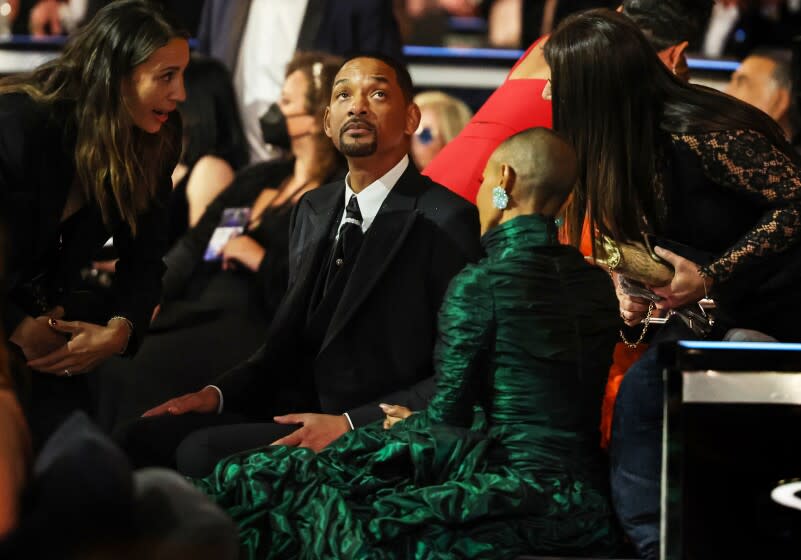 A man in a tuxedo and a woman in a green dress sitting in a crowd of people