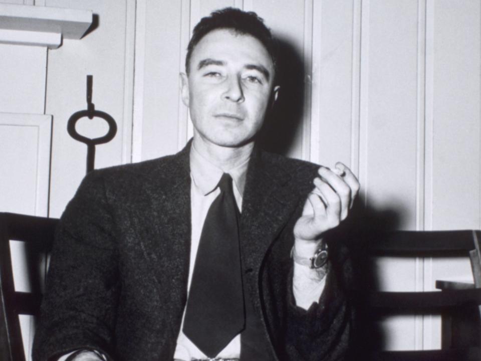 J. Robert Oppenheimer sits in a chair holding a cigarette.