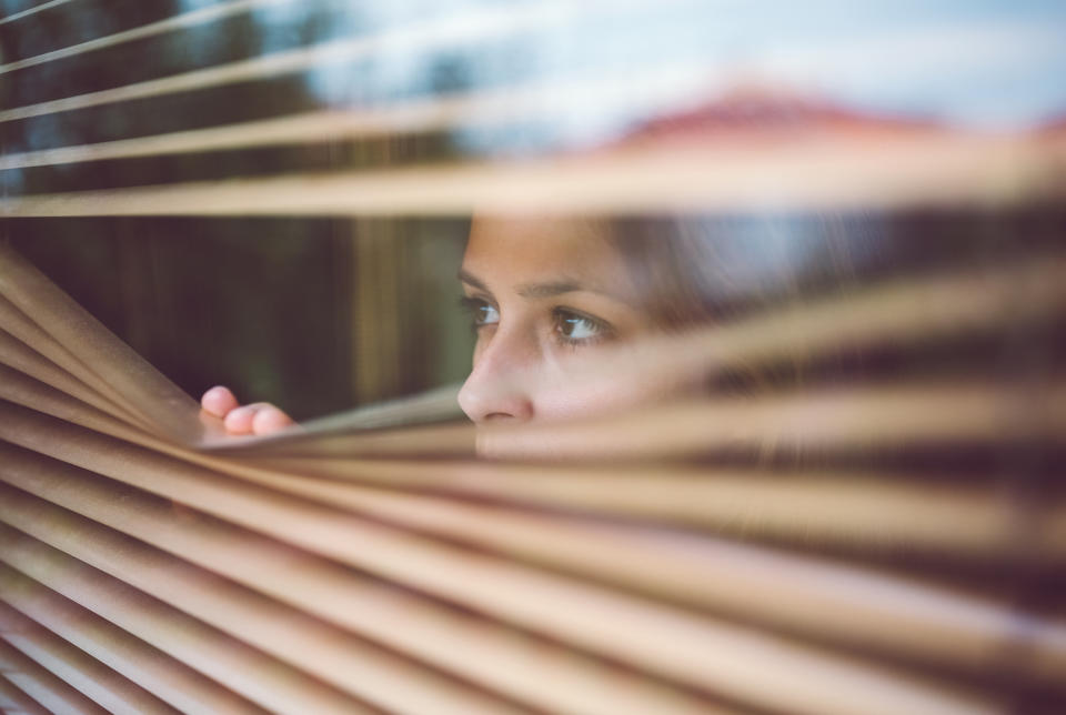 Stock image of a stalking victim looking nervous as she looks out of her window. (Getty Images)