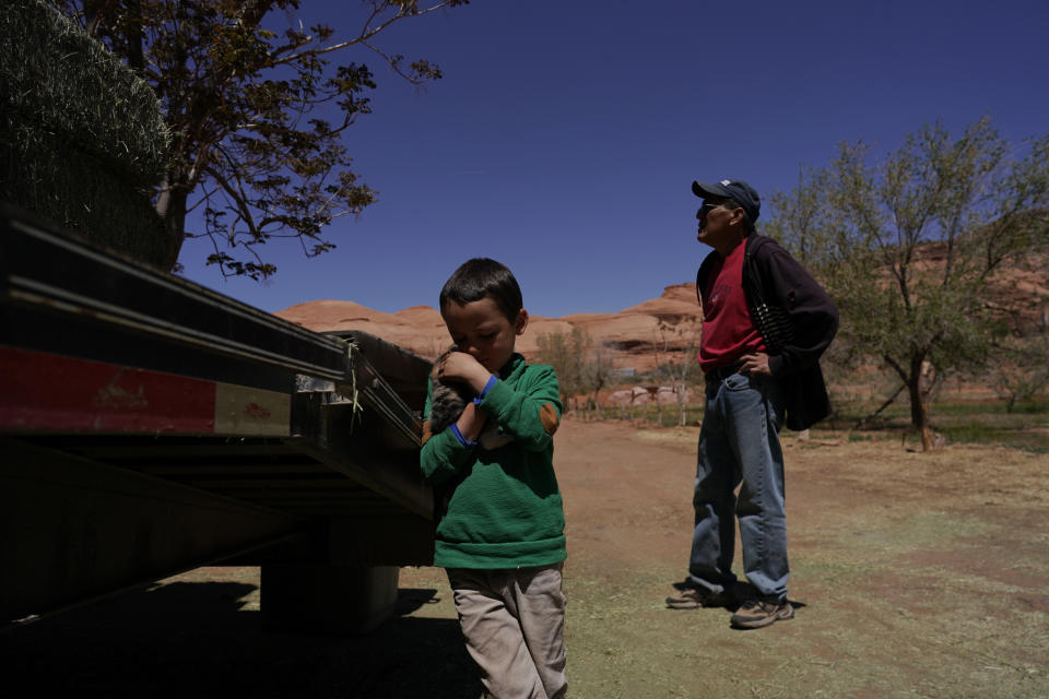 In this April 27, 2020, photo, Charlie Whitehouse, right, waits with a load of hay as a boy holds a kitten named Popcorn Ball in Oljato-Monument Valley, Utah, on the Navajo reservation. Even before the pandemic, people living in rural communities and on reservations were among the toughest groups to count in the 2020 census. (AP Photo/Carolyn Kaster)