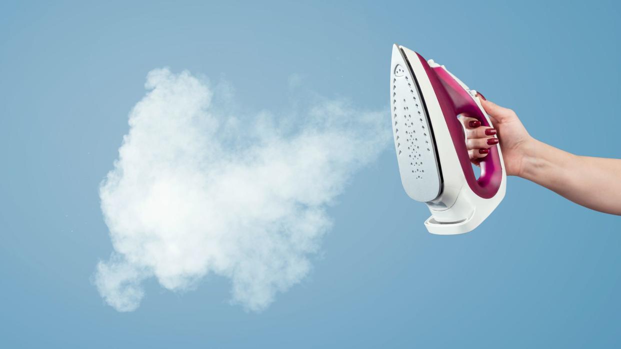  An iron emmits a jet of steam against a blue wall. 