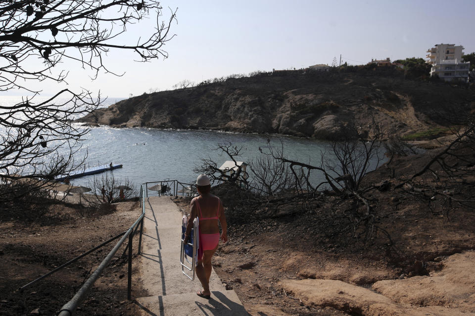 A woman walks towards a beach in Rafina, east of Athens, Wednesday, Aug. 1, 2018, ten days after the wildfire. The bodies of 76 people killed by Greece's deadliest wildfire in decades have been identified, authorities said Tuesday, as forensic experts kept working to identify more remains recovered from the charred resort area. (AP Photo/Thanassis Stavrakis)