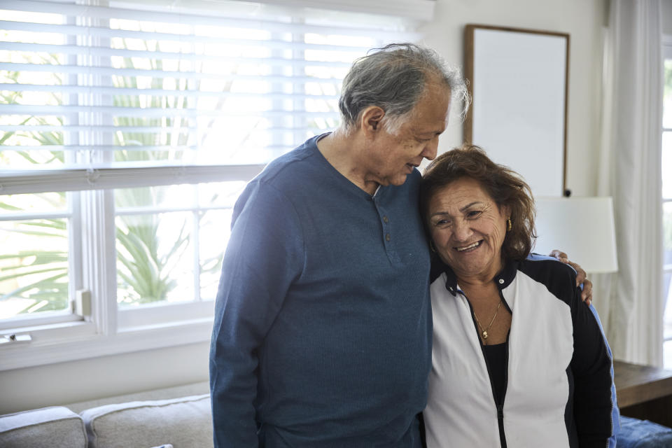 An older couple sharing an affectionate moment indoors, leaning on each other with smiles