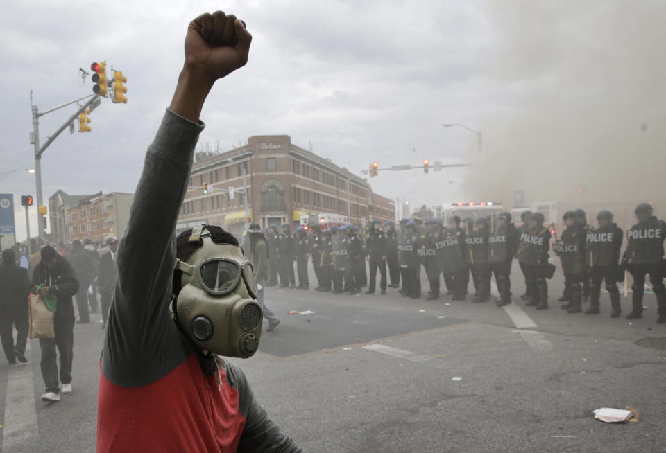 A demonstrator raises his fist as police stand in formation as a store burns, Monday, April 27, 2015, during unrest following the funeral of Freddie Gray in Baltimore. (AP Photo/Patrick Semansky)