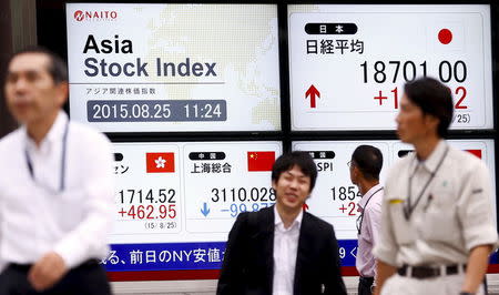 People walk past screens displaying market indices at a brokerage in Tokyo, August 25, 2015. REUTERS/Thomas Peter