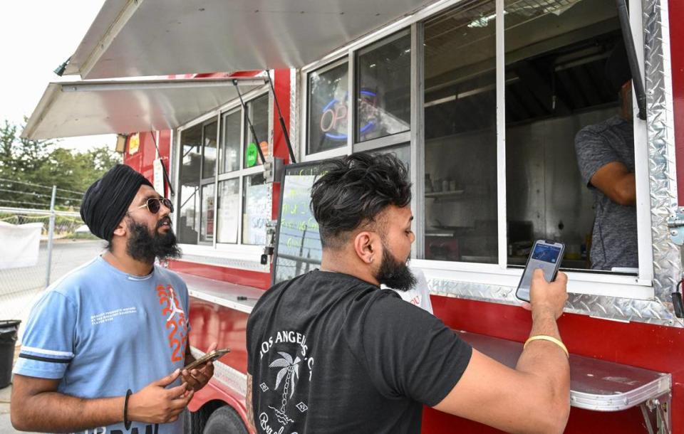 Customers Ramneek Singh, left, and Prince Singh give their orders at the Punjabi Chulla & Grill food truck on Shaw Avenue near Highway 99 in Fresno on Wednesday, Aug. 16, 2023.