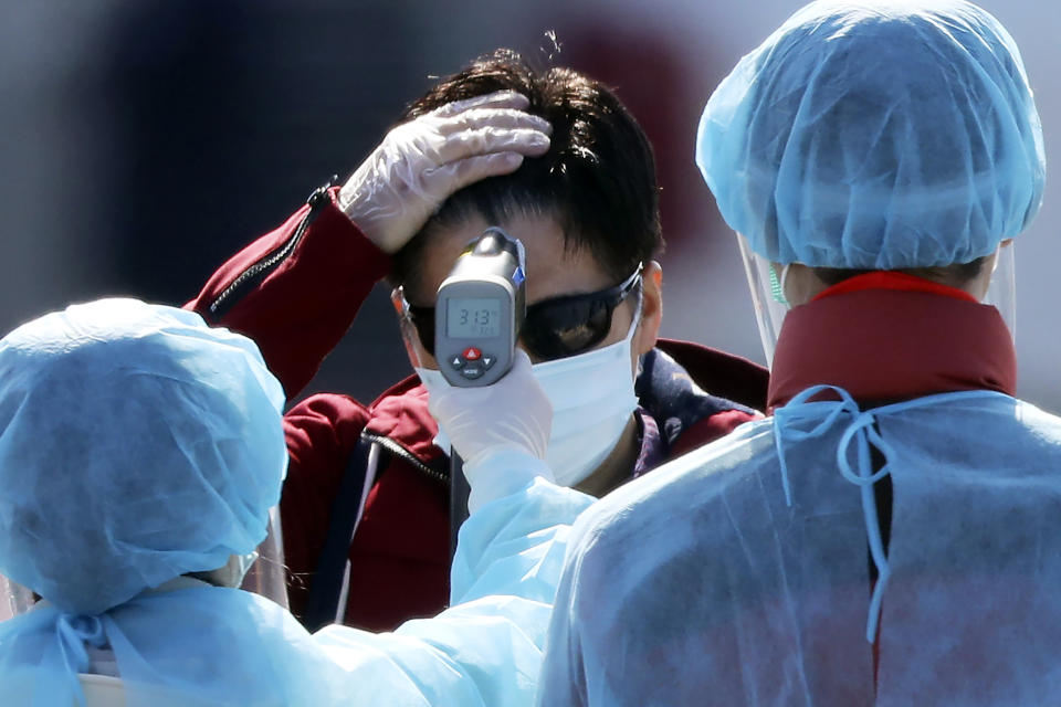 An official in protective suits measure the temperature of the foreign passengers disembarked from the quarantined Diamond Princess cruise ship before boarding to buses at a port in Yokohama, near Tokyo, Friday, Feb. 21, 2020. Japanese Prime Minister Shinzo Abe should be basking in the limelight this year in the runup to the 2020 Tokyo Olympics. Instead, the economy is reeling and criticism is mounting over his government's handling of a new virus that began in China and has spread alarmingly in Japan. (AP Photo/Eugene Hoshiko)