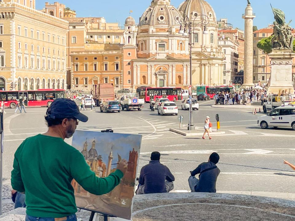 A man in Rome paints the 15th-century catholic chapel in front of him — Santa Maria di Loreto.