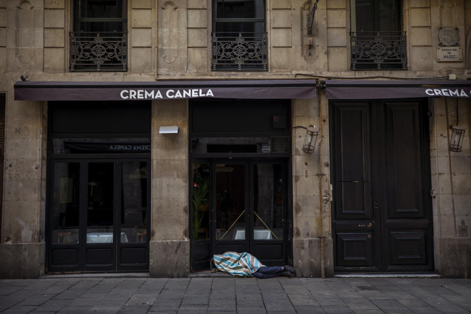 In this Saturday, March 21, 2020 photo, Jose sleeps in the street in downtown Barcelona, Spain. Jose, 27, has been sleeping in the street for 5 years and is convinced that the Spanish army will put all the beggars of the city in tents "I refuse! I am not going to be infested with the virus anywhere, I am safe here in the arcade". Authorities are scrambling to get as many homeless people off the streets without cramming them into a shelter, where the spread of COVID-19 could be even greater. (AP Photo/Emilio Morenatti)