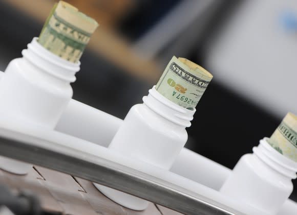 Plain white bottles on a manufacturing line, with rolled twenty dollar bills sticking out the top of them.