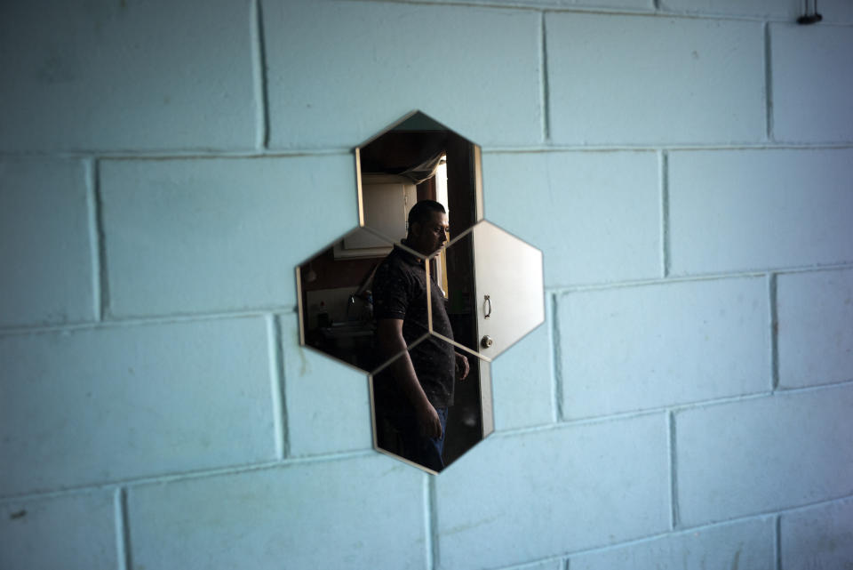 In this June 19, 2019, photo, Juan Carlos Perla is reflected in a mirror along the wall of their temporary home in Tijuana, Mexico. The Perla family of El Salvador has slipped into a daily rhythm in Mexico while they wait for the U.S. to decide if they will win asylum. A modest home replaced the tent they lived in at a migrant shelter. (AP Photo/Gregory Bull)