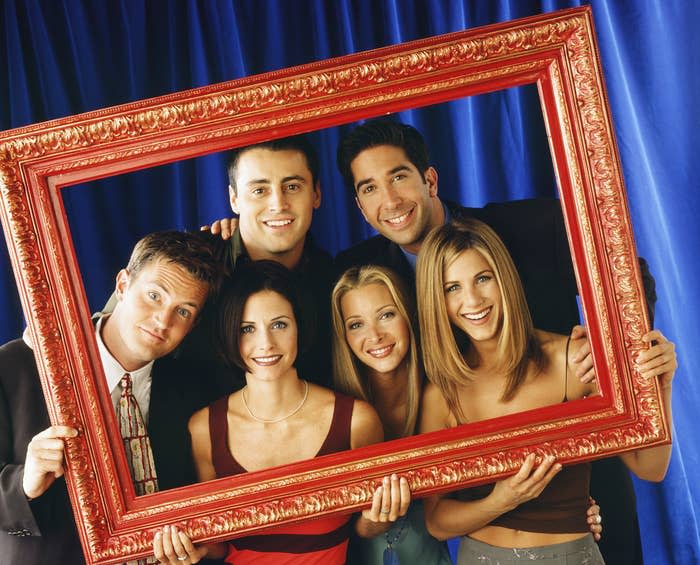 The whole cast poses while holding a red frame around themselves