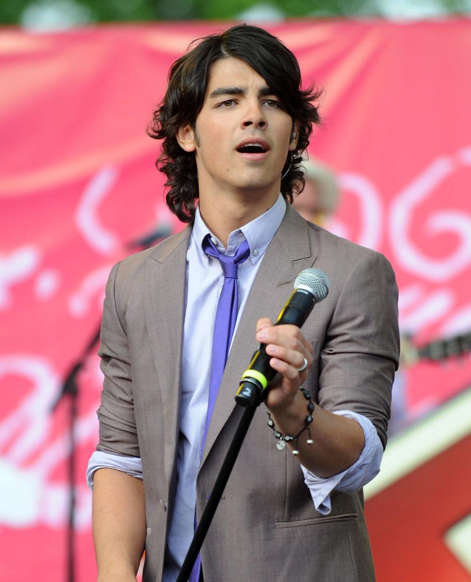 Joe Jonas performing onstage in a loose suit and tie