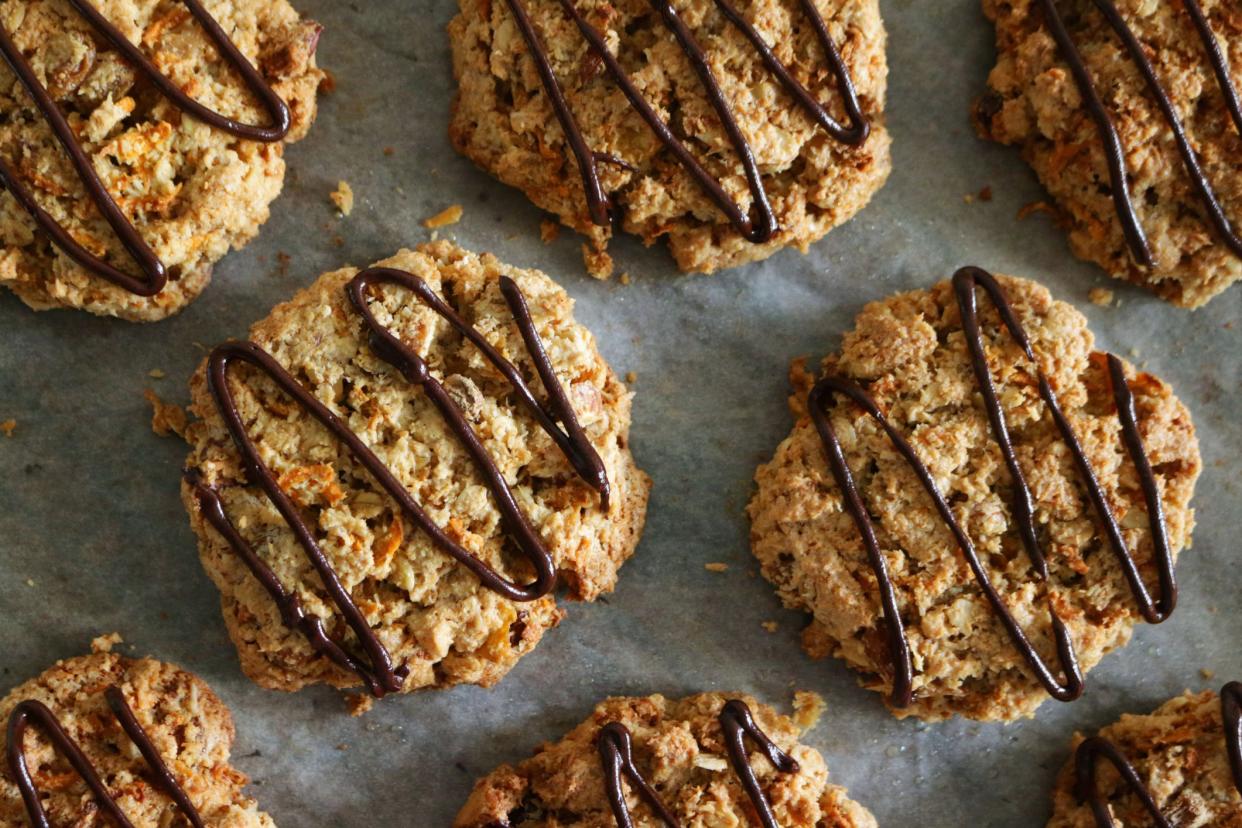 Stock photo showing an elevated view of greaseproof paper lined baking oven tray containing freshly baked, homemade carrot, coconut and chocolate chip biscuits, home baking concept.