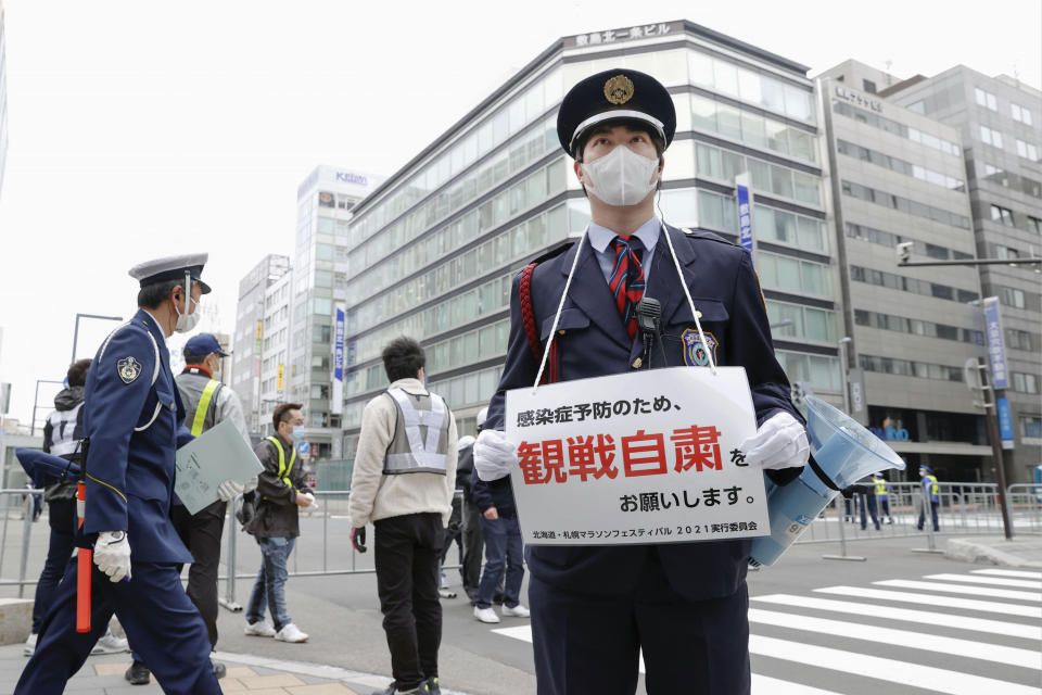 A security guard stands with a note calling for refraining from watching a half-marathon to help curb the spread of the coronavirus in Sapporo, northern Japan, Wednesday, May 5, 2021. The half-marathon was held as a Tokyo 2020 test event three months before the Olympics open. (Masanori Takei/Kyodo News via AP)