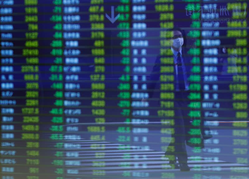 A man wearing protective face mask, following an outbreak of the coronavirus, is reflected on a screen displaying stock prices outside a brokerage in Tokyo