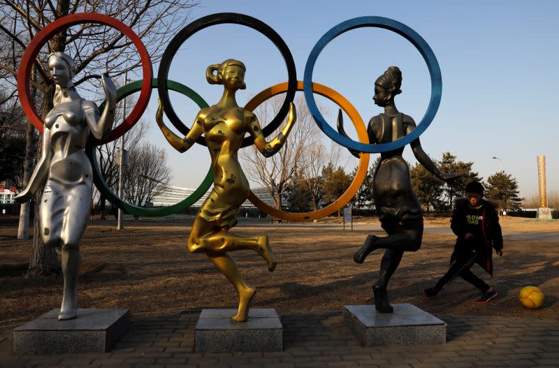 Child plays football near a statue of Olympic rings at the Olympic Forest Park in Beijing