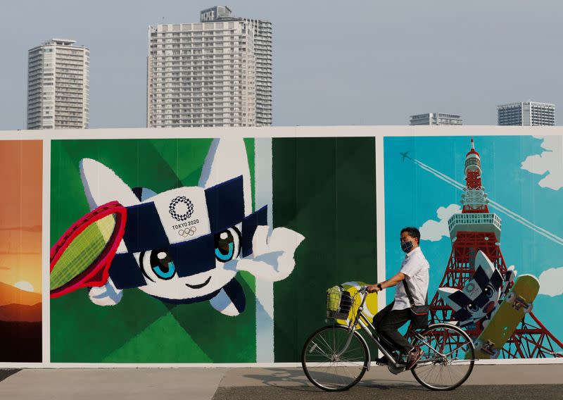 FILE PHOTO: A man wearing a protective mask rides his bicycle past a large poster featuring Tokyo 2020 Olympic Games mascot Miraitowa amid the coronavirus disease (COVID-19) outbreak in Tokyo