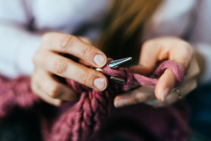 Close-up of hands knitting with chunky yarn, creating a pink textile