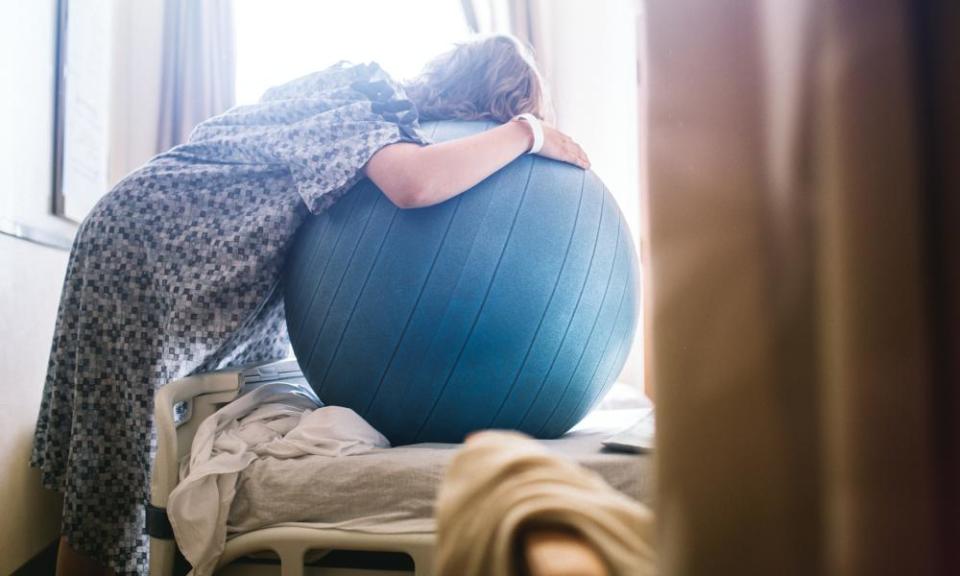 Pregnant Woman in Hospital BedA woman in labor prepares to give birth in a clean white hospital setting. She leans on a birthing or fitness ball to ease the intensity of her contractions. A depiction of a positive pregnancy and delivery.