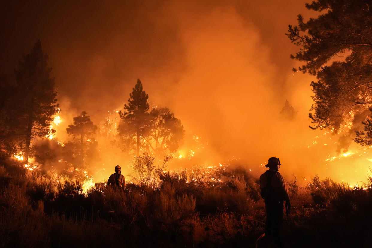 Two firefighters watch the Bridge Fire burn near a structure in Wrightwood, Calif., on Tuesday.