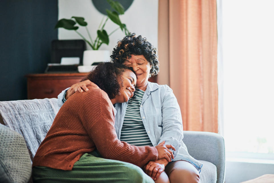 Adult daughter hugging her mother on a couch, both smiling with eyes closed, expressing love and comfort