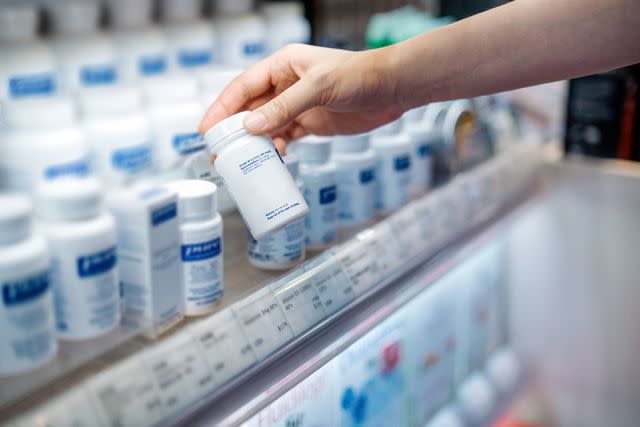 <p>d3sign / Getty Images</p> Female's hand takes a bottle of medicine from a pharmacy shelf
