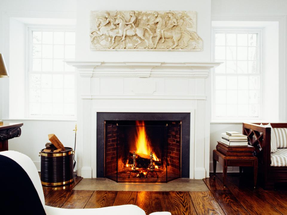 A living room with white and brown furniture, wooden floors, and a fireplace with a fire lit.