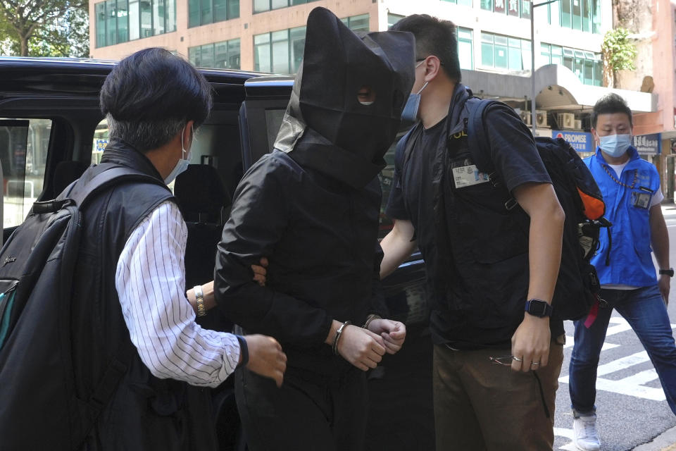 A hooded suspect is accompanied by police officers to search evidence at office in Hong Kong Thursday, July 22, 2021. Hong Kong's national security police on Thursday arrested five people from a trade union of the General Association of Hong Kong Speech Therapists on suspicion of conspiring to publish and distribute seditious material, in the latest arrests made amid a crackdown on dissent in the city. (AP Photo/Vincent Yu)