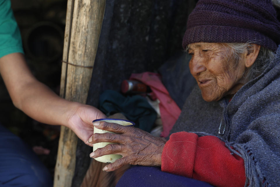 In this May 11, 2020 photo, 80-year-old Dominga Aduviri is handed a cup of soda from her “adopted” grandson Wilmer Gutierrez, in La Paz, Bolivia. Gutierrez is determined to sort out his “adopted” grandmother’s problems. (AP Photo/Juan Karita)