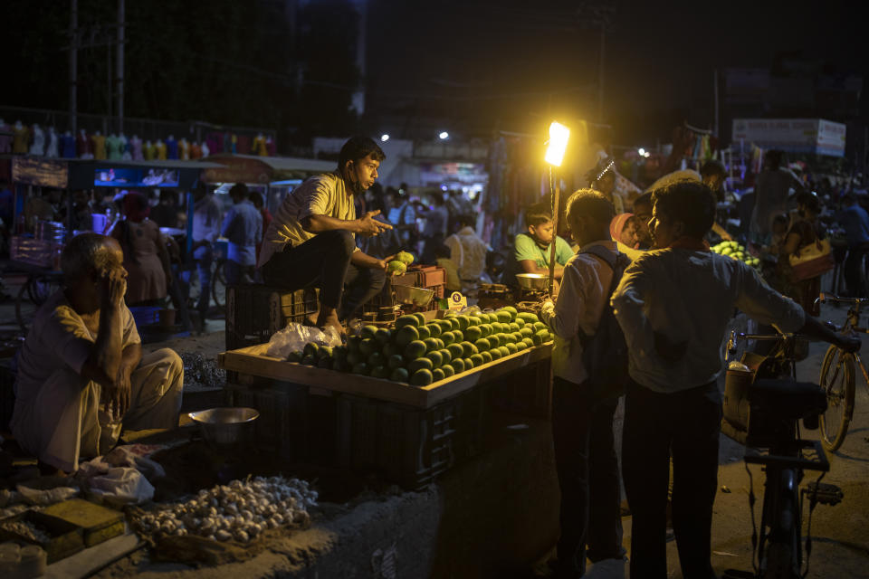 Un vendedor de fruta habla con los clientes de su puesto, todos sin mascarilla, en un mercado nocturno en Noida, a las afueras de Nueva Delhi, India, el 16 de julio de 2020. (AP Foto/Altaf Qadri)