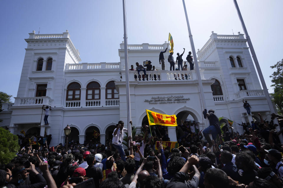 A protester, carrying national flag, stands with others on top of the building of Sri Lankan Prime Minister Ranil Wickremesinghe's office, demanding he resign after president Gotabaya Rajapaksa fled the country amid economic crisis in Colombo, Sri Lanka, Wednesday, July 13, 2022. Rajapaksa fled on a military jet on Wednesday after angry protesters seized his home and office, and appointed Prime Minister Ranil Wickremesinghe as acting president while he is overseas. Wickremesinghe quickly declared a nationwide state of emergency to counter swelling protests over the country's economic and political collapse. (AP Photo/Eranga Jayawardena)