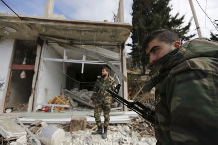 Forces loyal to Syria's President Bashar al-Assad stand in front of damaged shops in the town of Rabiya after they recaptured the rebel-held town in coastal Latakia province, Syria January 27, 2016. REUTERS/Omar Sanadiki