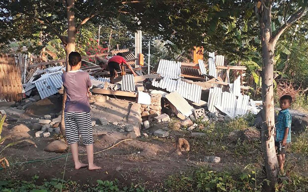 An Indonesian person scrambles over the collapsed ruins of a house as others look on following an earthquake in Lombok - AFP