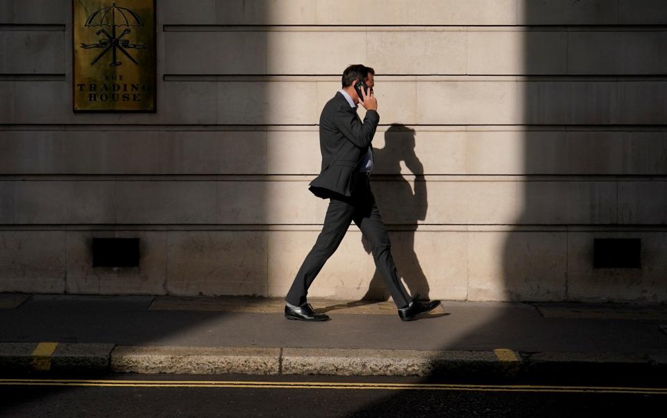 A man talks on the phone as he walks through the City of London's financial district