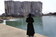 A priest looks towards the towering grain silos, that were gutted in the massive explosion last August, where a Mass will be held to commemorate the first year anniversary of the deadly blast, in Beirut seaport, Lebanon, Wednesday, Aug. 4, 2021. The grim anniversary comes amid an unprecedented economic and financial meltdown and a political stalemate that has kept the country without a functioning government for a full year. (AP Photo/Hussein Malla)