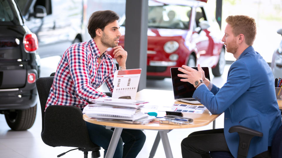 car agent talking with male customer at car dealership saloon.