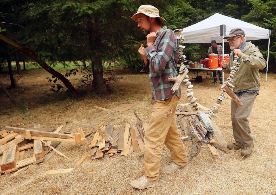 Artist Thomas Dambo, left, and volunteer Tom Nordlie, of Poulsbo, carry a necklace of shells and driftwood to the troll called "Pia the Peacekeeper" to test out the length of the accessory in Sakai Park on Bainbridge Island, Wash. on Friday, Aug. 18, 2023.