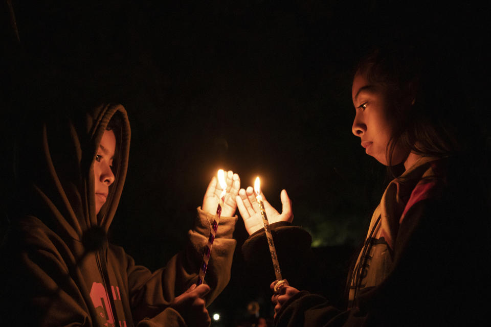 Youths hold candles over a tomb at a cemetery in Atzompa, Mexico, late Tuesday, Oct. 31, 2023. In a tradition that coincides with All Saints Day and All Souls Day on Nov. 1 and Nov. 2, families decorate the graves of departed relatives with flowers and candles, and spend the night in the cemetery, eating and drinking as they keep company with their deceased loved ones. (AP Photo/Maria Alferez)