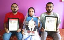 Anindita Mitra, 61, flanked by her sons Satyajit Mitra, right and Abhijit Mitra, pose with portraits of her husband late Narayan Mitra, at her house in Silchar, India, Sunday, Sept. 13, 2020. Narayan Mitra, wasn't listed among those killed by the coronavirus that authorities put out daily because the test results confirming COVID-19 arrived after his death. In India, people who die with other preexisting conditions are often not counted as COVID-19 deaths, while only those who test positive for the virus before dying are included in the official tally in many states. (AP Photo/Joy Roy)