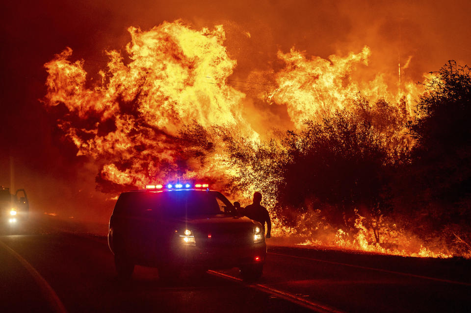 Flames lick above vehicles on Highway 162 as the Bear Fire burns in Oroville, Calif., on Wednesday, Sept. 9, 2020. The blaze, part of the lightning-sparked North Complex, expanded at a critical rate of spread as winds buffeted the region. (AP Photo/Noah Berger)