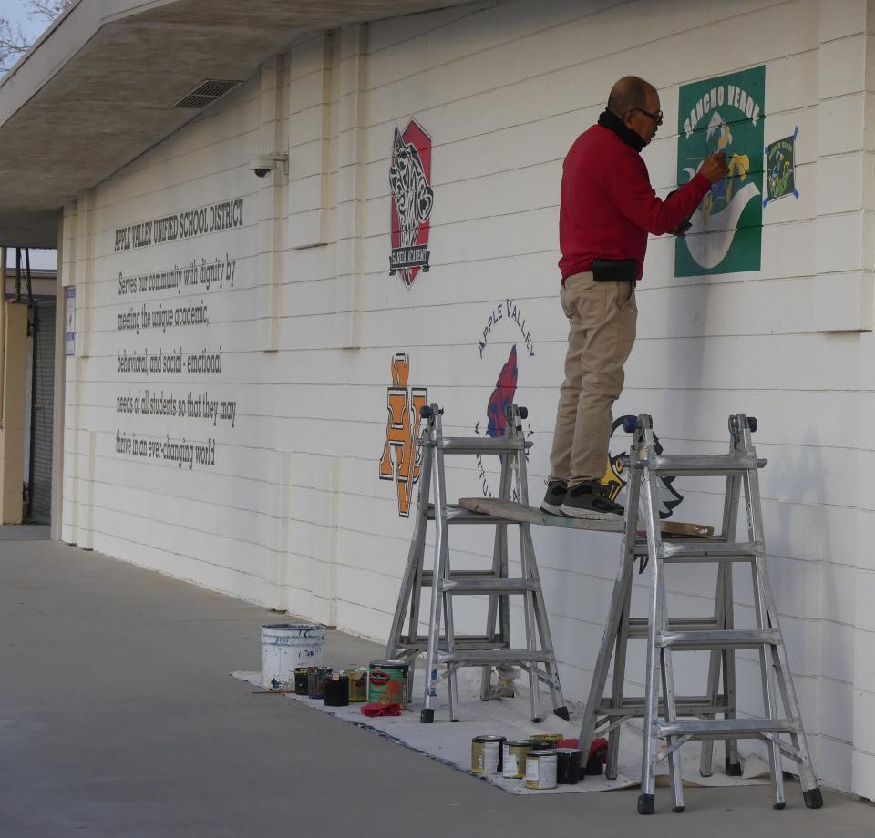 Business owner Miguel Gonzalez continues painting by hand, over a dozen school logos for the Apple Valley Unified School District.