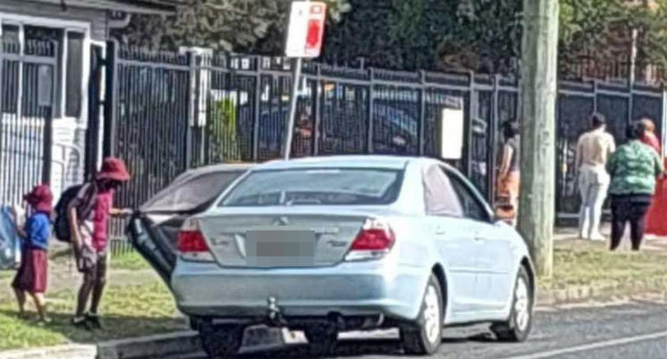 A car is parked outside a school in Taree as people stand on the footpath.