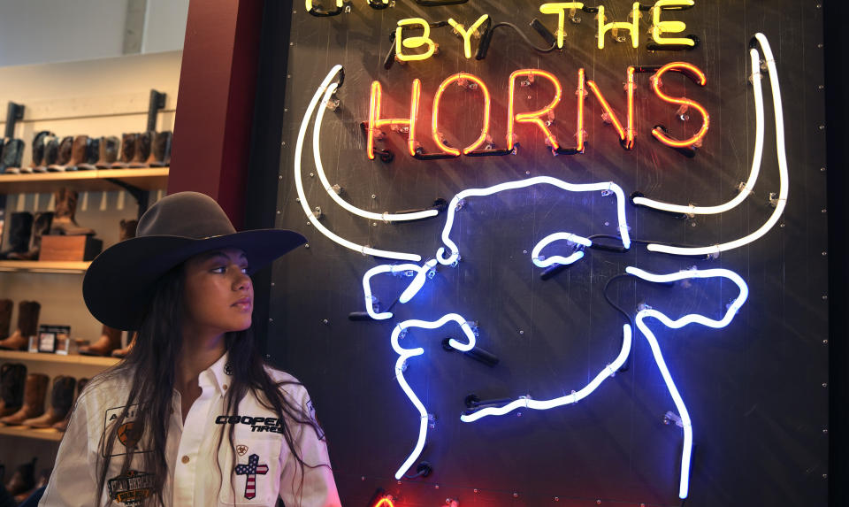 Bull rider Najiah Knight looks at neon lights showing a bull in an Ariat store, one of her current sponsors, in the Fort Worth Stockyards, Wednesday, Oct. 4, 2023, in Fort Worth, Texas. Najiah, a high school junior from small-town Oregon, is on a yearslong quest to become the first woman to compete at the top level of the Professional Bull Riders tour. (AP Photo/LM Otero)