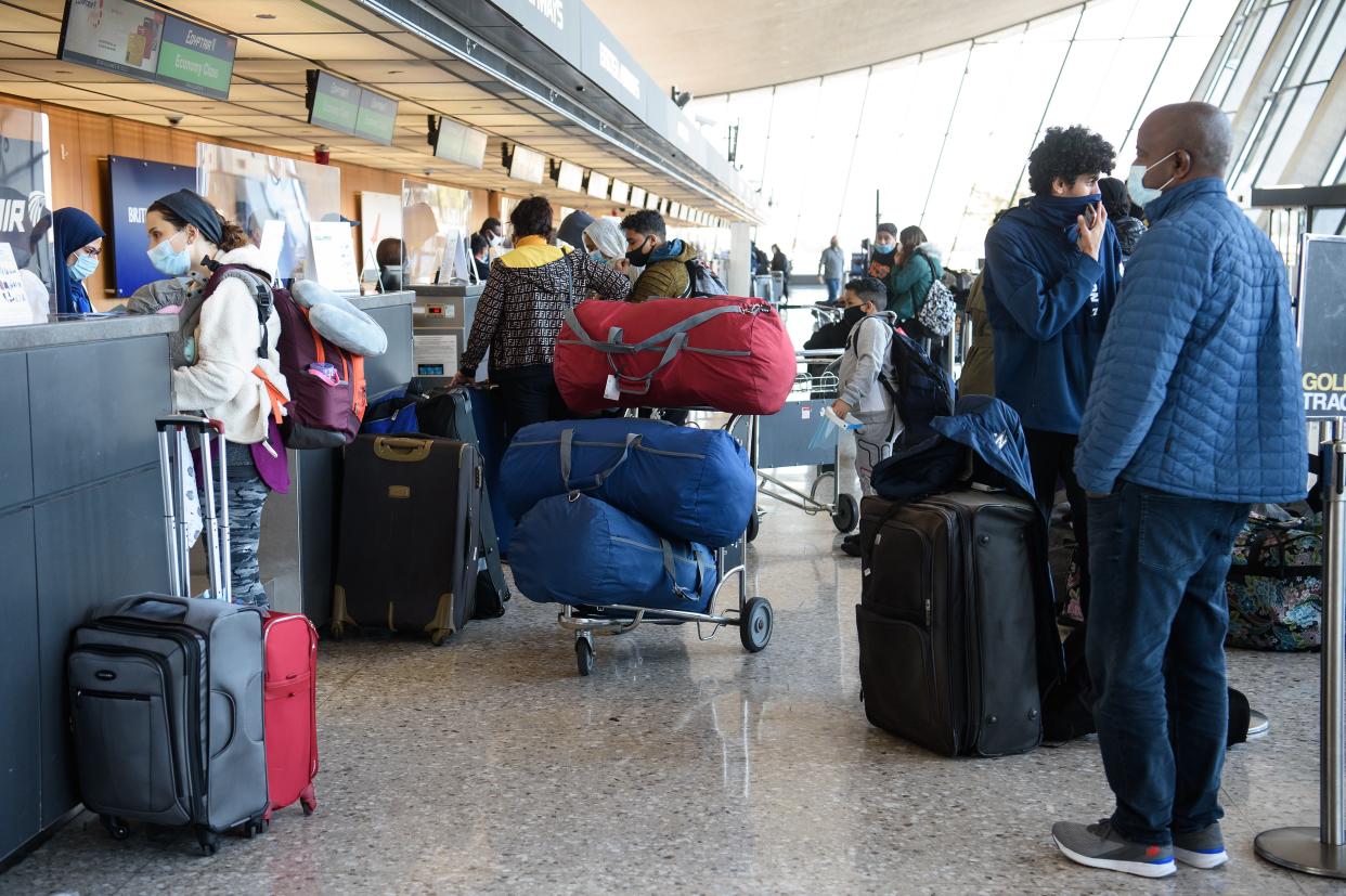 Travelers in face masks stand at a check-in counter surrounded by luggage at Dulles International Airport in Dulles, Va.