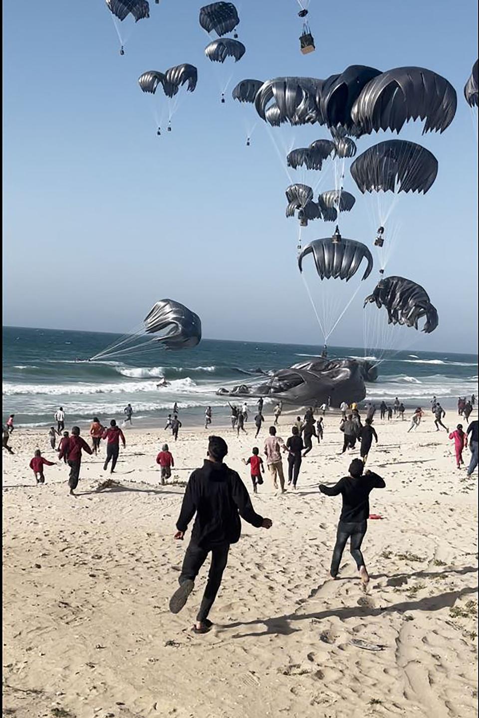 This image grab from an AFPTV video shows Palestinians running toward parachutes attached to food parcels, air-dropped from U.S. aircraft on a beach in the Gaza Strip on March 2, 2024.