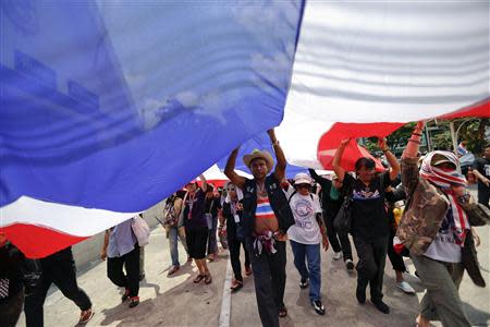 Anti-government protesters carry a large national flag as they arrive for the funeral service of their slain comrade at a Buddhist temple in Bangkok April 2, 2014. Gunmen opened fire on a group of Thai anti-government protesters driving away from a Bangkok rally on Tuesday, killing one, wounding four and raising tension in a political crisis that has gripped the country for months. REUTERS/Damir Sagolj